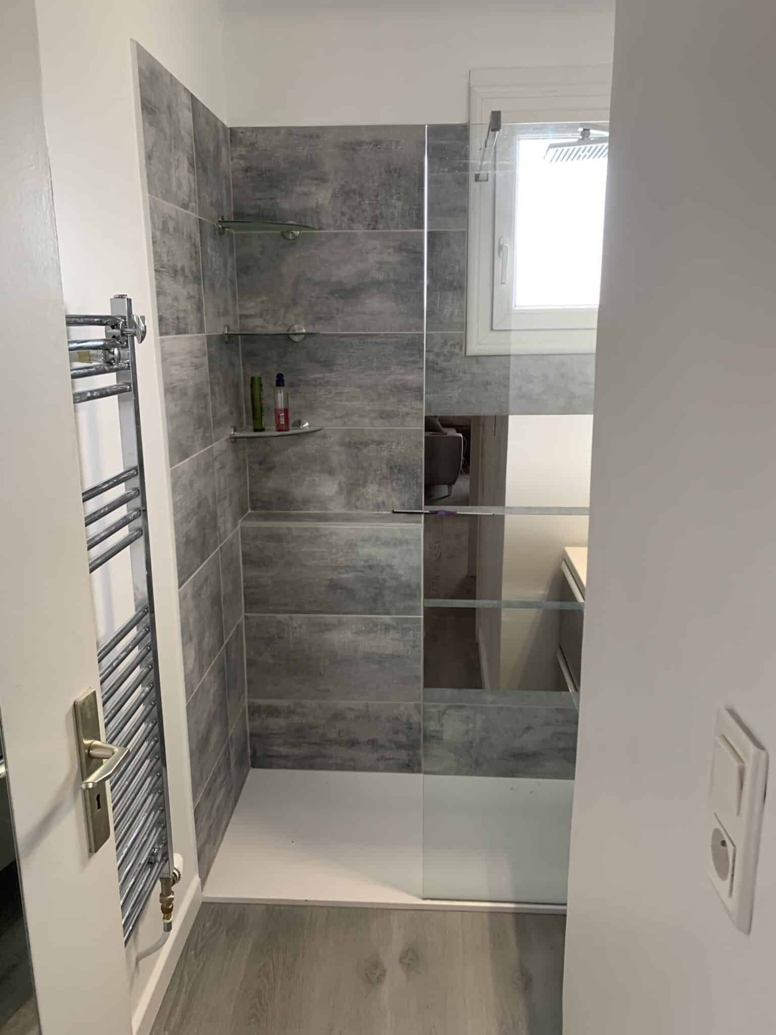 Salle de bain moderne avec douche carrelée et panneau vitré.