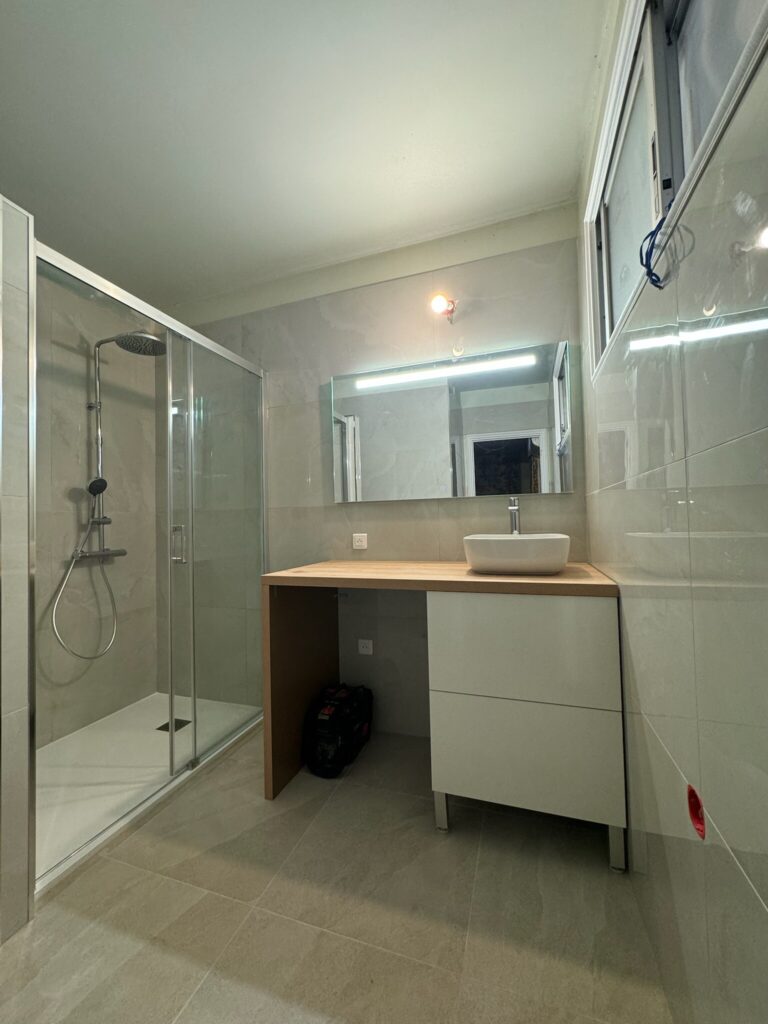Salle de bains moderne avec douche vitrée et lavabo.