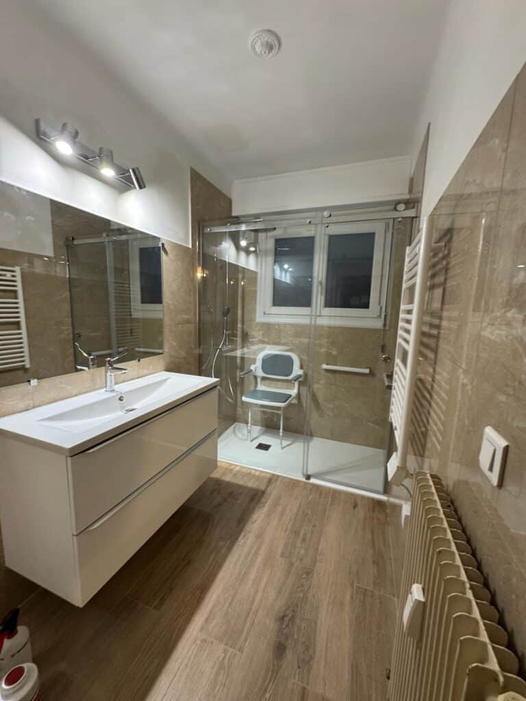 Salle de bain moderne avec douche, lavabo et sol bois.