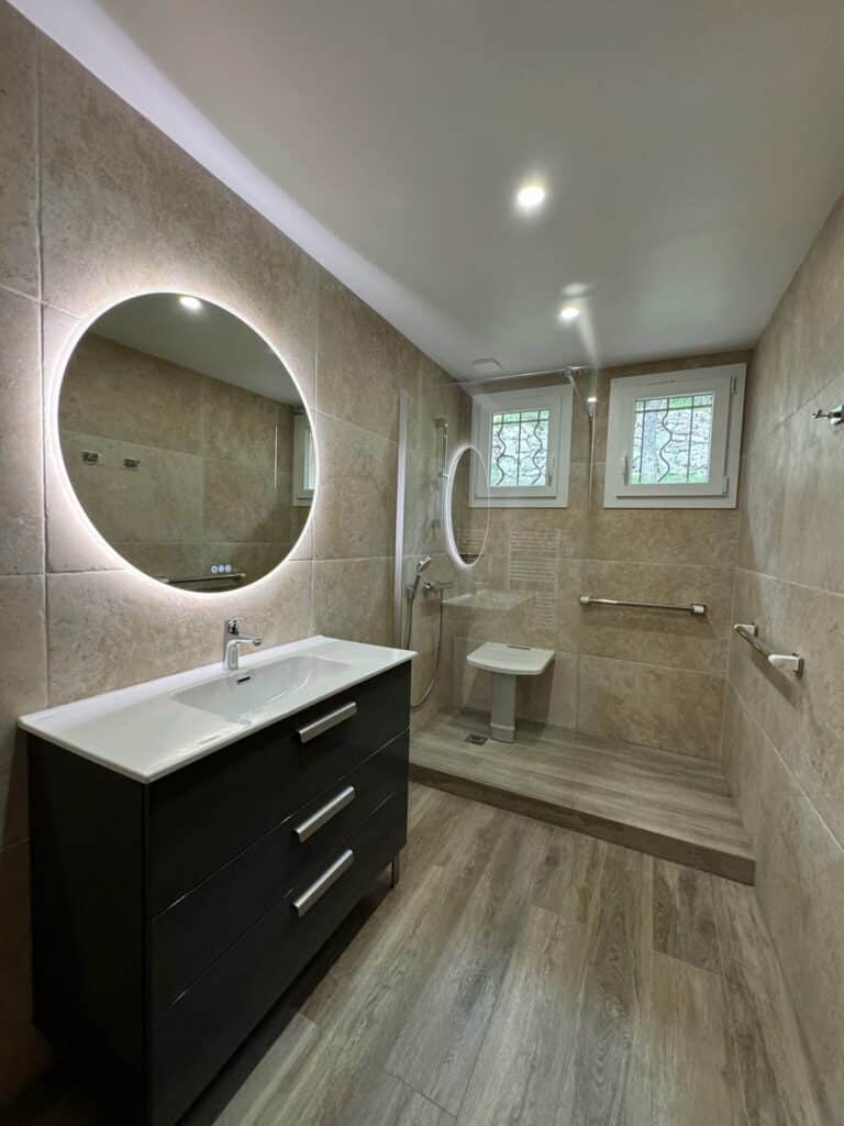 Salle de bains moderne, miroir circulaire, douche à l'italienne. Fenêtres au-dessus de la douche.