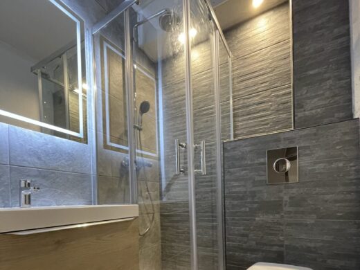 Salle de bains moderne à Grasse : douche vitrée, WC suspendu, meuble en bois. Carrelage gris raffiné.