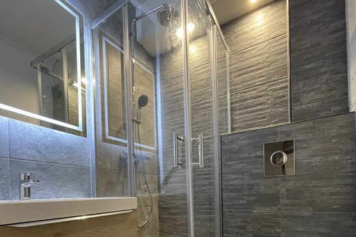 Salle de bain moderne : douche en verre, lavabo mural, armoire miroir, WC suspendu, carrelage gris.