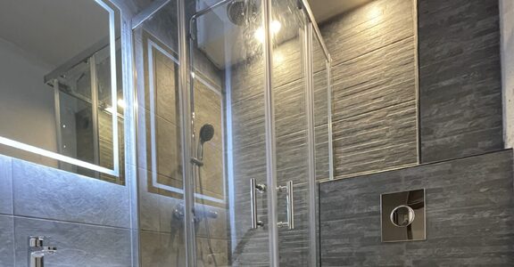 Salle de bain moderne : douche en verre, lavabo mural, armoire miroir, WC suspendu, carrelage gris.